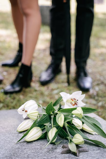 A bouquet of fresh white lilies with large green leaves and unopened buds resting on a stone surface. The lilies have open petals revealing their orange and brown stamens, while the buds are tightly c