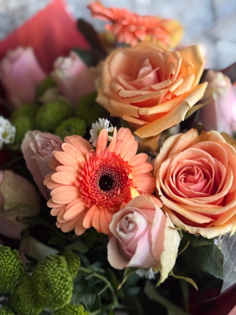 A close-up view of a floral arrangement featuring a variety of fresh flowers including peach-colored roses with tightly packed petals, a light pink rose partially open, and a peach-orange gerbera dais